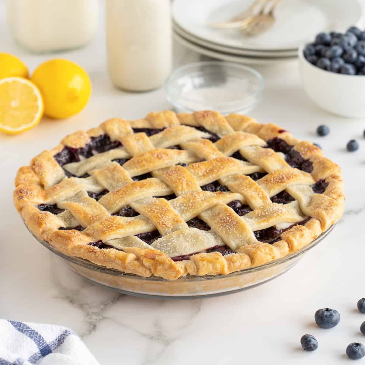 A blueberry pie with a lattice crust on a white kitchen counter.