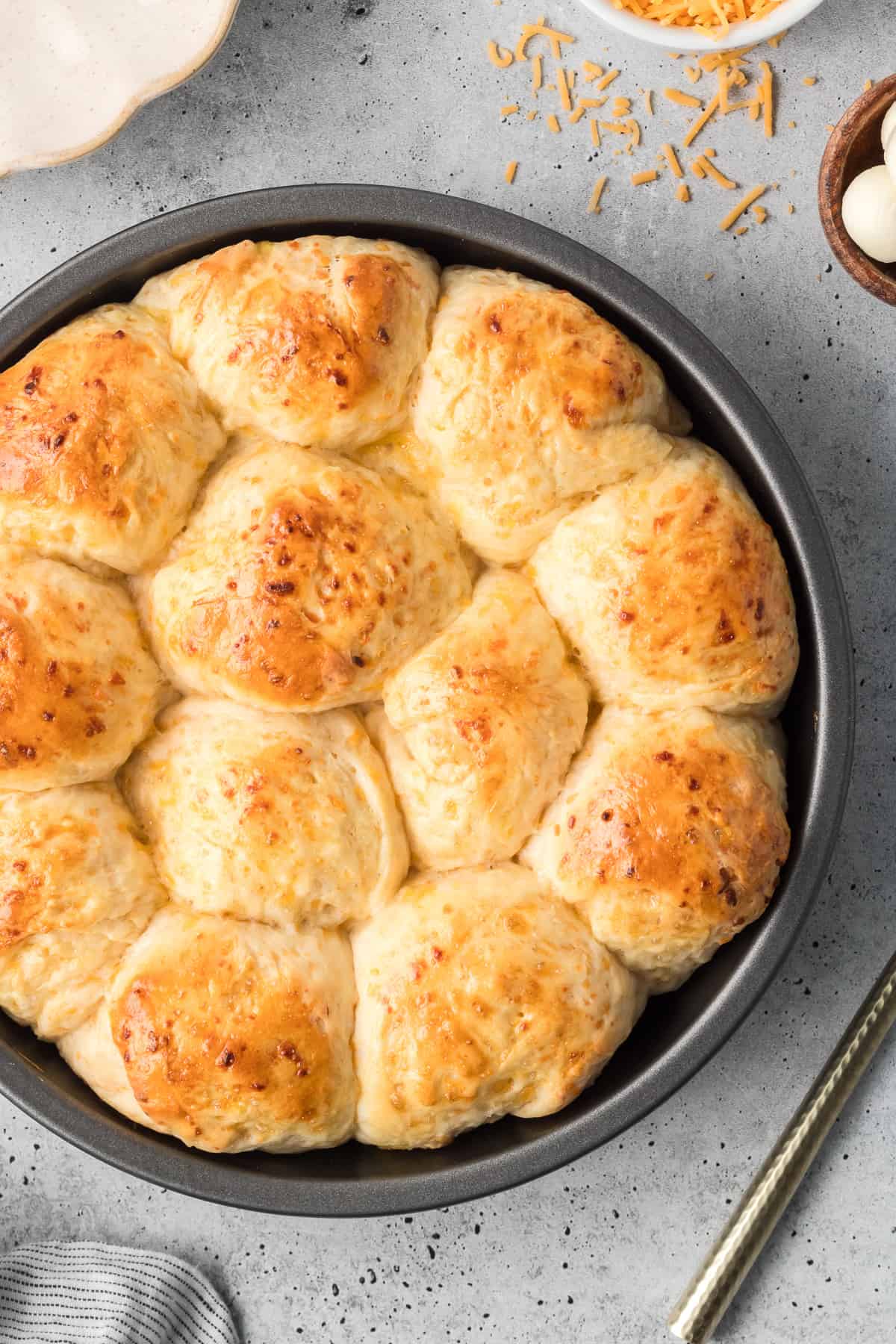 A top down shot of cheddar dinner rolls in a round metal cake pan.