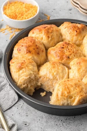 A metal cake pan filled with cheddar rolls with one missing.