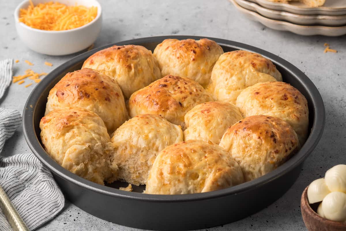 A metal cake pan filled with cheddar rolls with one missing.