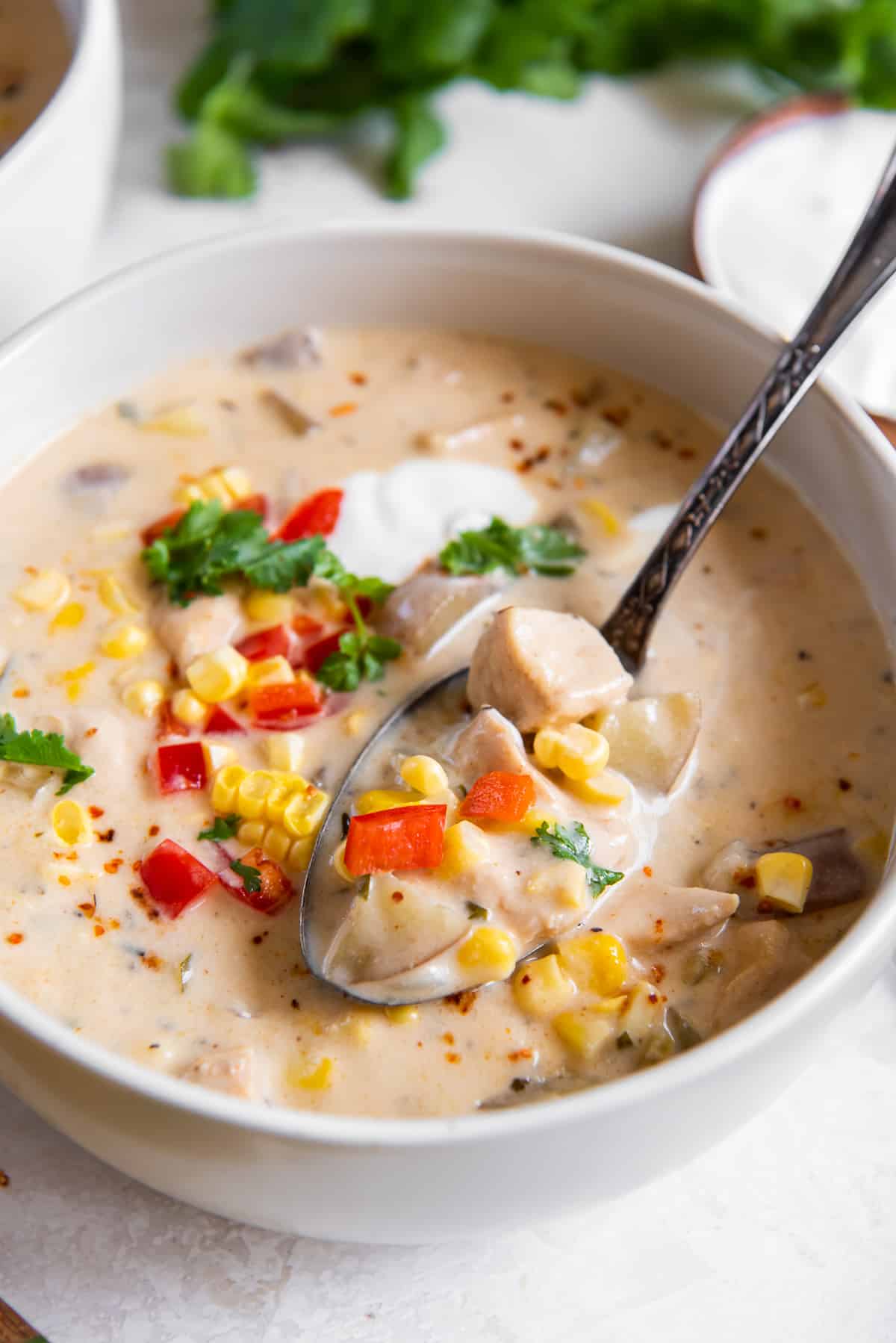 A spoon scooping up chicken corn chowder from a bowl.