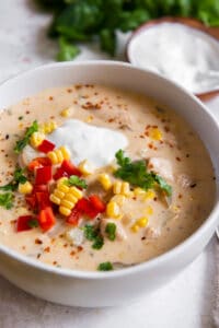 A close up of a bowl of chicken corn chowder topped with sour cream and diced bell peppers.