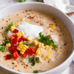 A close up of a bowl of chicken corn chowder topped with sour cream and diced bell peppers.