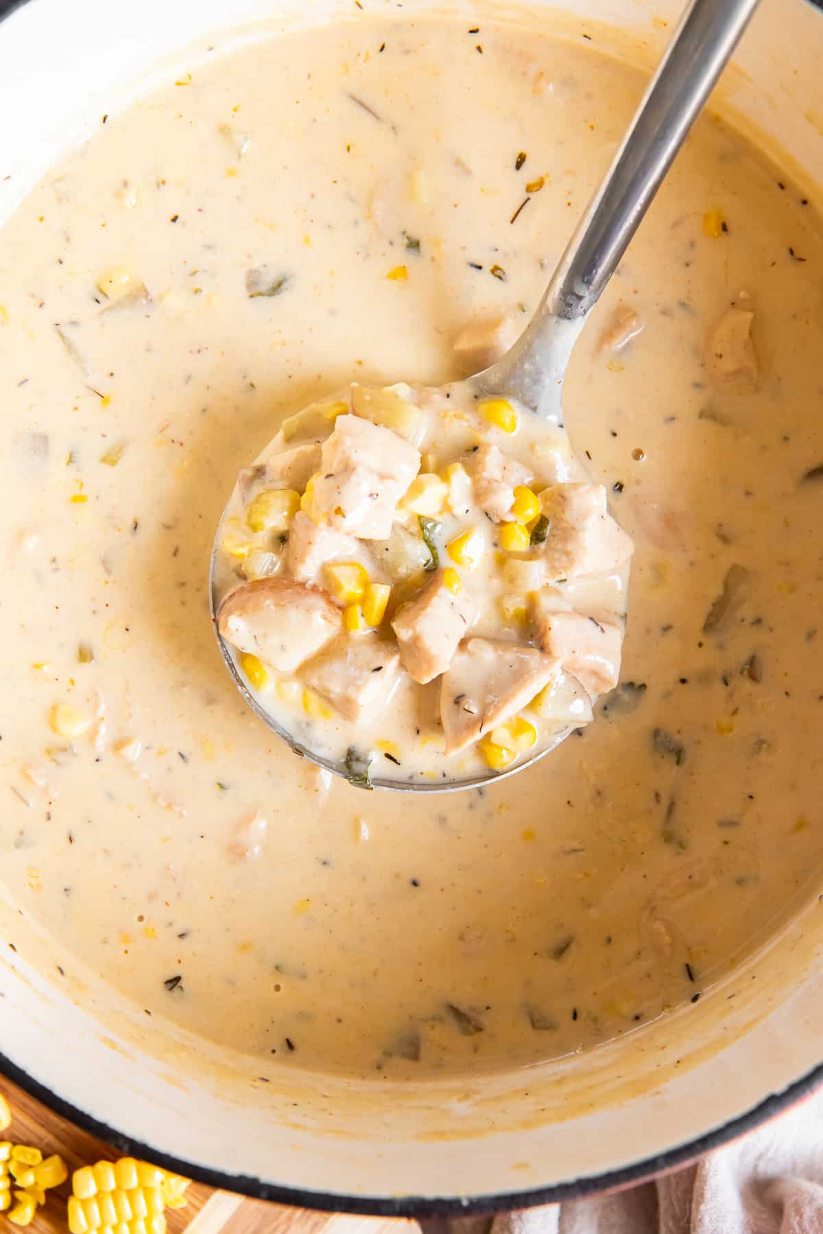 A top down close up shot of a ladle hovering above a pot of chicken corn chowder.