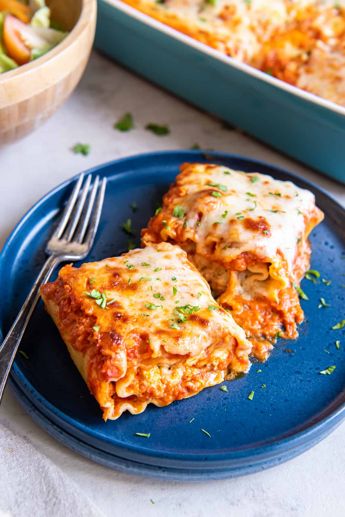 Two chicken lasagna roll ups on a blue plate with a fork.