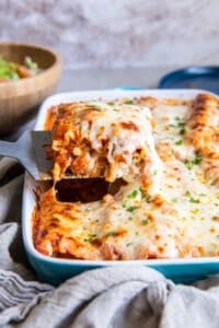 A spatula lifting a cheesy chicken lasagna rollup from a baking dish.