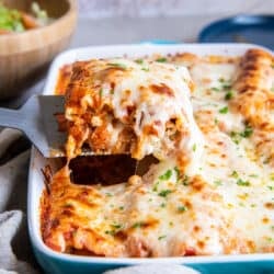 A spatula lifting a cheesy chicken lasagna rollup from a baking dish.