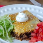 A serving of crescent roll filled with taco filling on a plate with shredded lettuce and diced tomato.