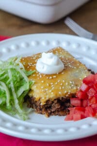 A serving of crescent roll filled with taco filling on a plate with shredded lettuce and diced tomato.