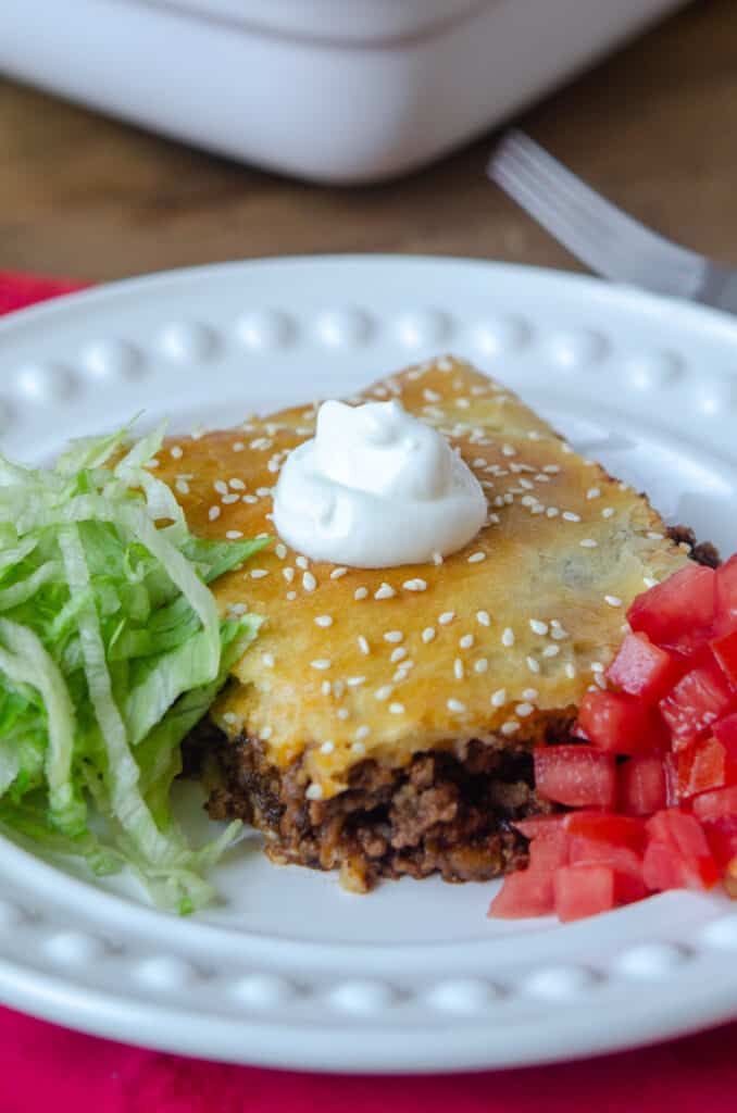 A serving of crescent roll filled with taco filling on a plate with shredded lettuce and diced tomato.