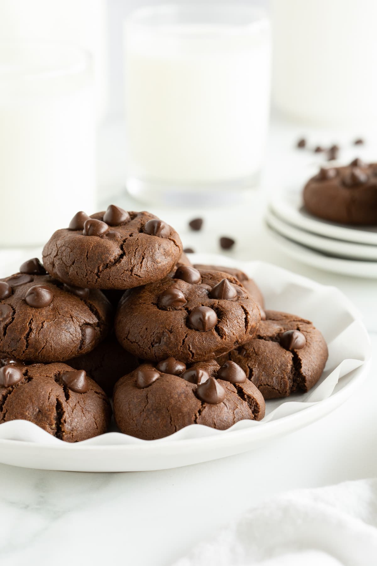 A stack of chocolate cookies with chocolate chips on a white plate.
