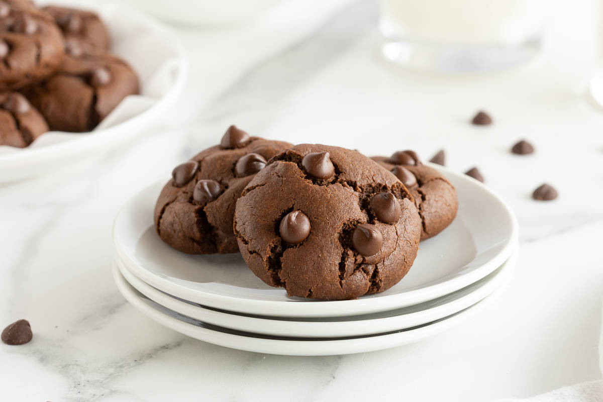 Three double chocolate cookies on a stack of three white plates.