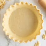 A top down shot of an unbaked pie crust with a fluted edge next to a rolling pin and scraps of pie pastry.