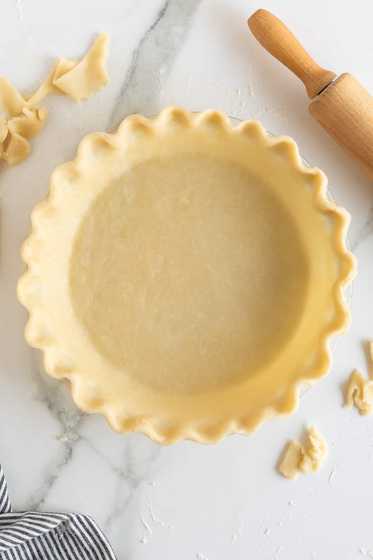 A top down shot of an unbaked pie crust with a fluted edge next to a rolling pin and scraps of pie pastry.