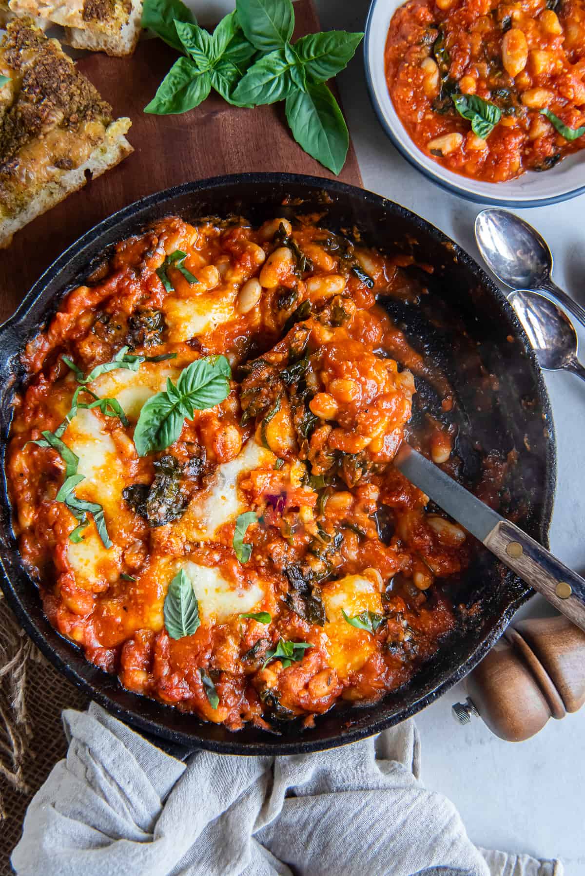 A top down shot of a spoon resting in a cast iron skillet filled with Italian Beans.