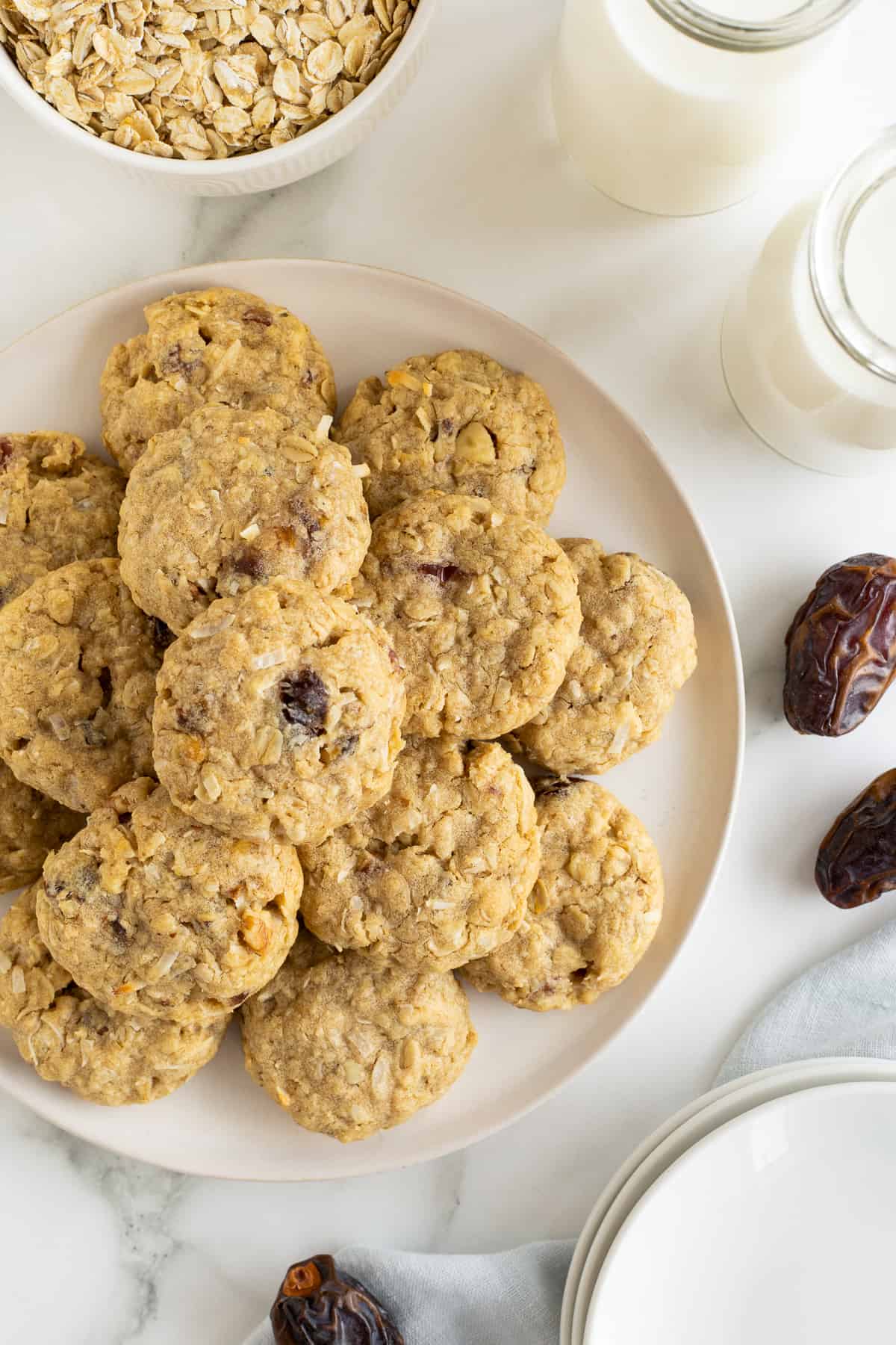 A top down shot of Oatmeal Date Cookies stacked on a white plate on a kitchen counter.