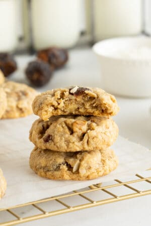 Three Oatmeal Date Cookies stacked on a wire rack with a bite missing from the one on top.