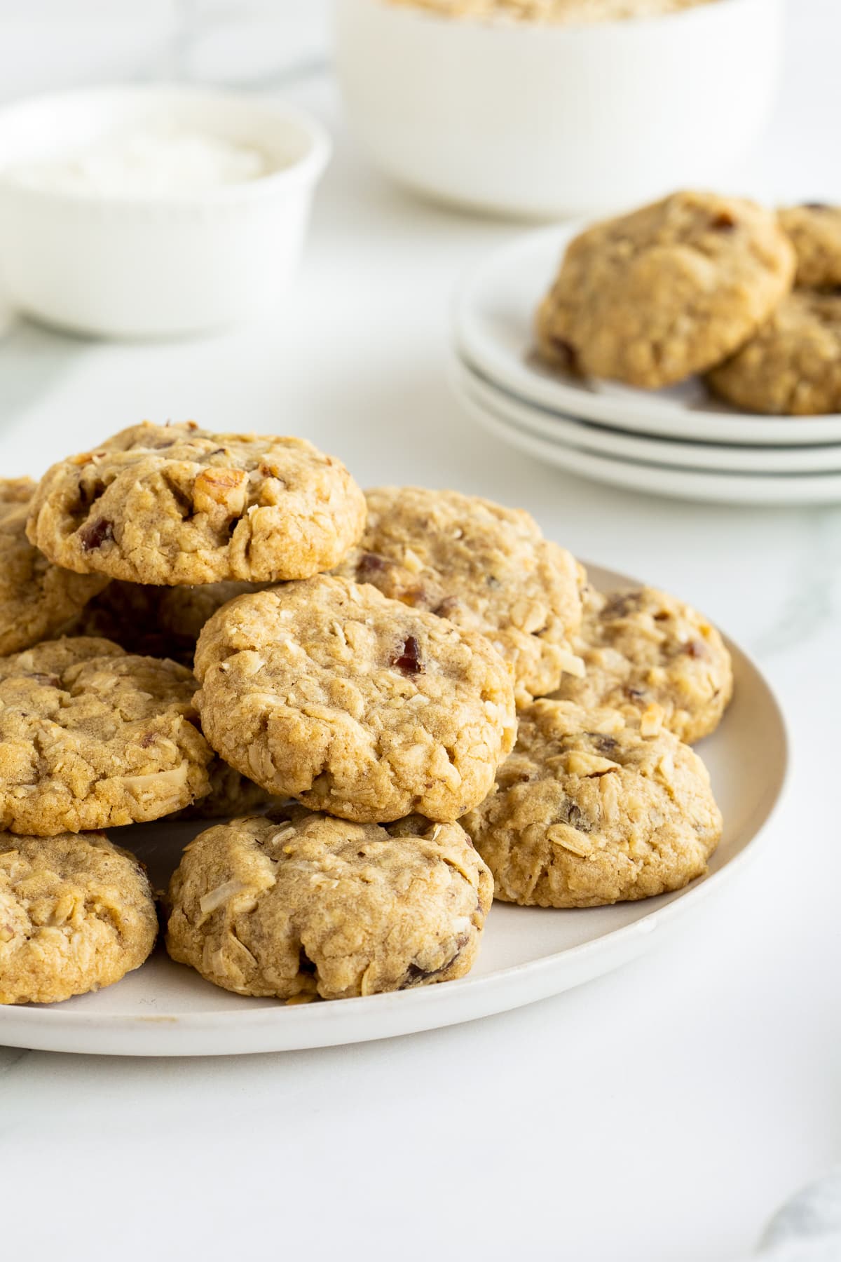 Oatmeal Date Cookies stacked on a white plate on a kitchen counter.