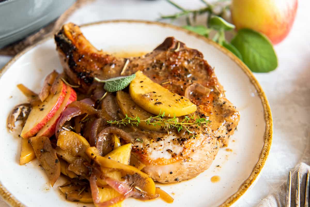 A side view close up of a pork chop on a dinner plate topped with sauce, apples, and onions.