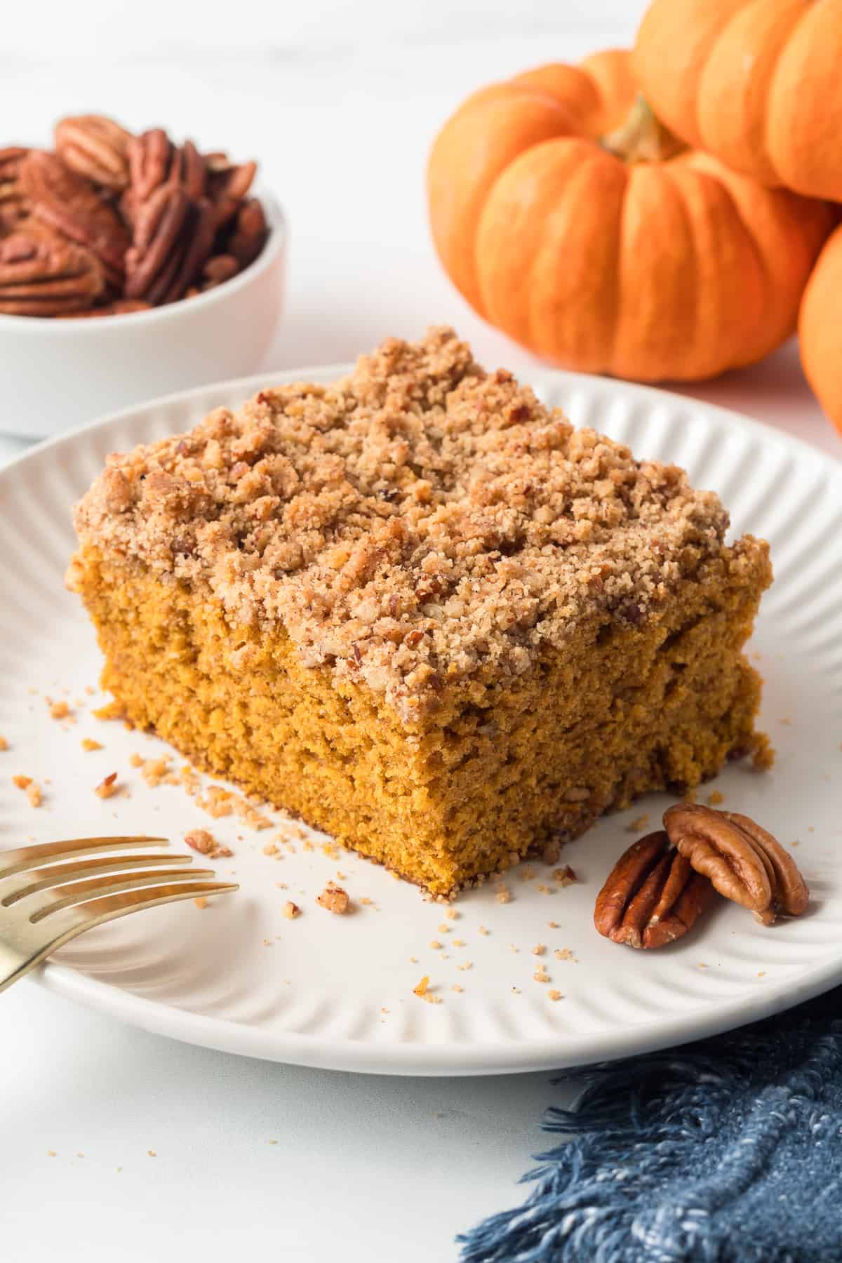 A slice of pumpkin crumb cake on a white plate with two pecans and a fork.