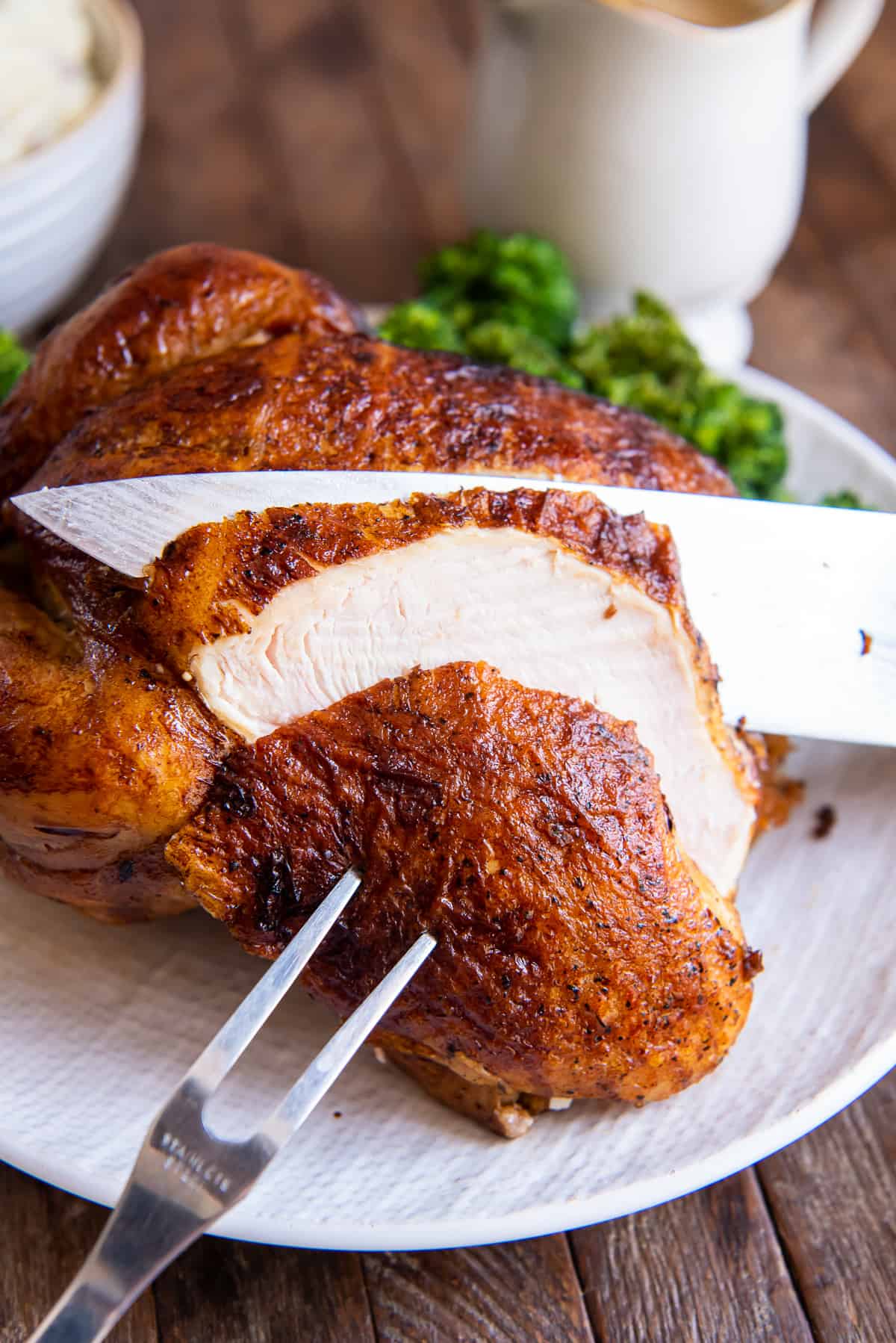 A fork stuck into a slice of chicken while a knife slices through behind it.