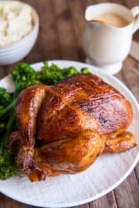 A rotisserie chicken on a white platter with sprigs of fresh parsley.