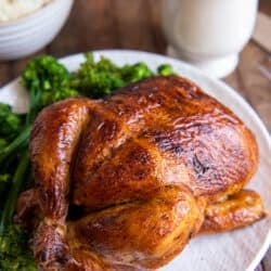 A rotisserie chicken on a white platter with sprigs of fresh parsley.