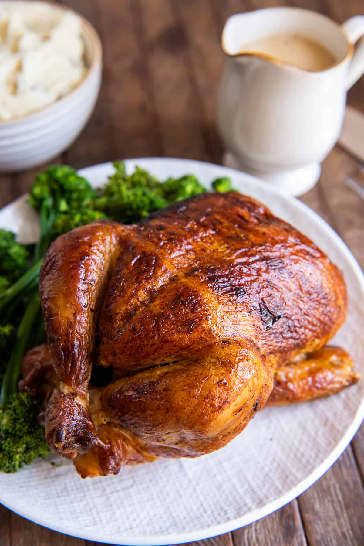 A rotisserie chicken on a white platter with sprigs of fresh parsley.