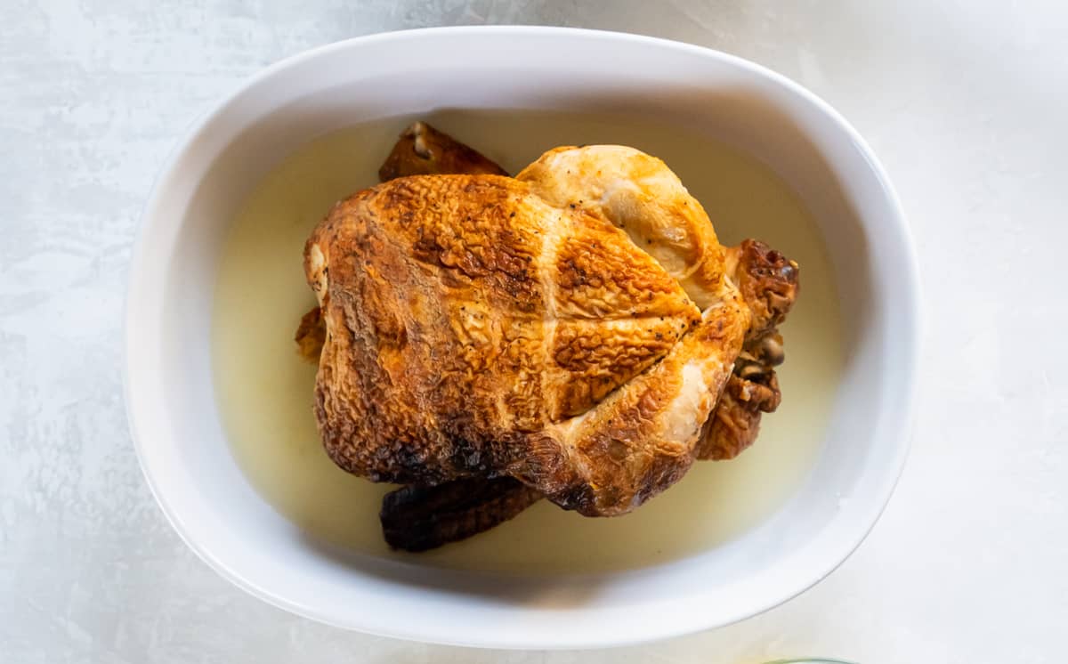 A top down shot of a rotisserie chicken in a baking dish with chicken broth.