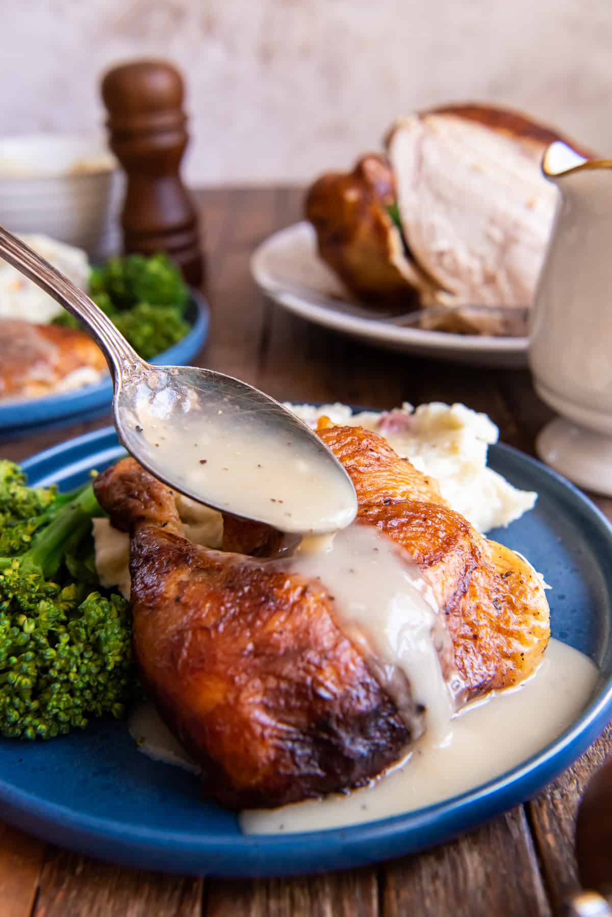 Gravy pouring from a spoon over a piece of rotisserie chicken on a blue plate.
