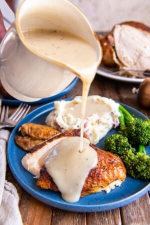 Gravy pouring from a gravy boat on to a piece of rotisserie chicken on a blue plate.