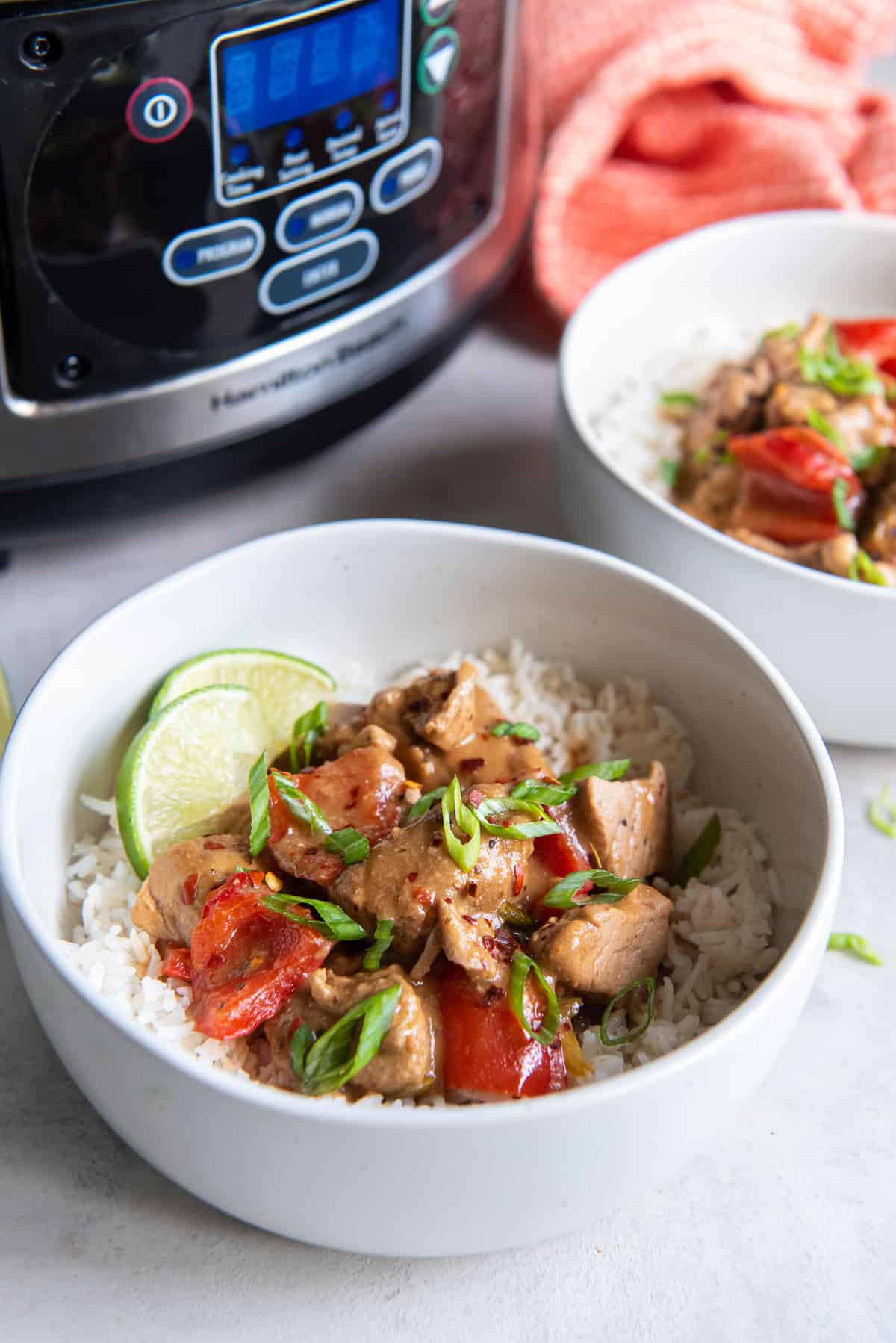 Two bowls filled with rice and pork with peppers in front of a slow cooker.