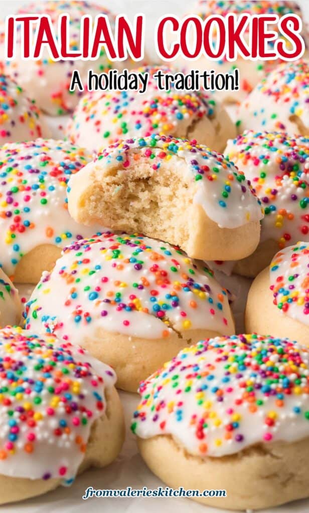A close up of a pile of Italian Cookies with icing and rainbow sprinkles with a bite missing from the cookie on top with text.