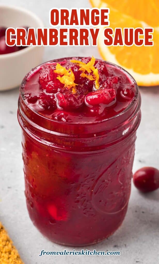 A small mason jar filled with cranberry sauce and topped with orange zest with text.