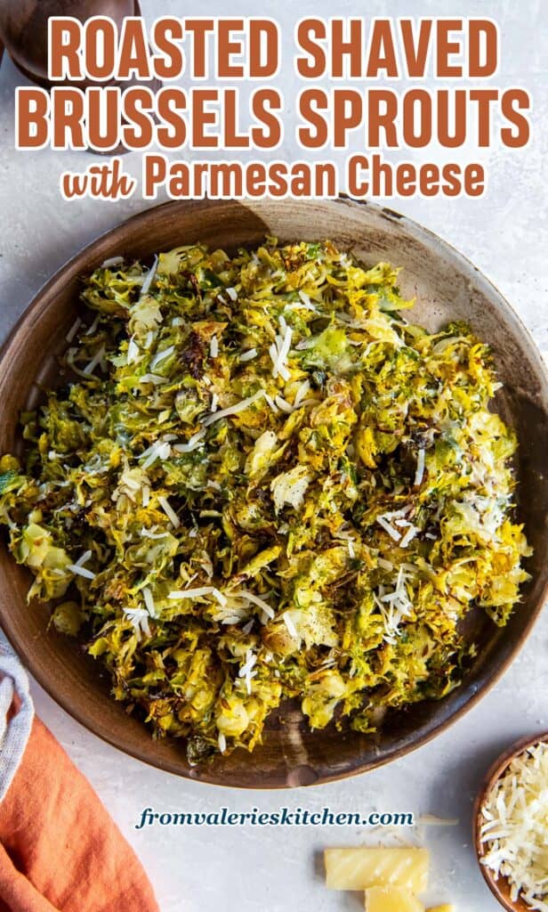 Roasted shredded Brussels sprouts in a wooden bowl next to salt and pepper shakers and a small bowl of shredded Parmesan with text.