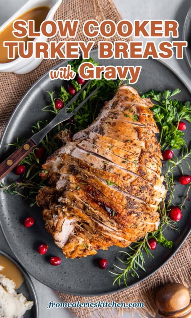 A top down shot of a sliced slow cooker turkey breast on a grey platter with cranberries and fresh herbs with text.