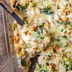 A spoon scooping chicken stuffing bake with broccoli and cheese from a baking dish.