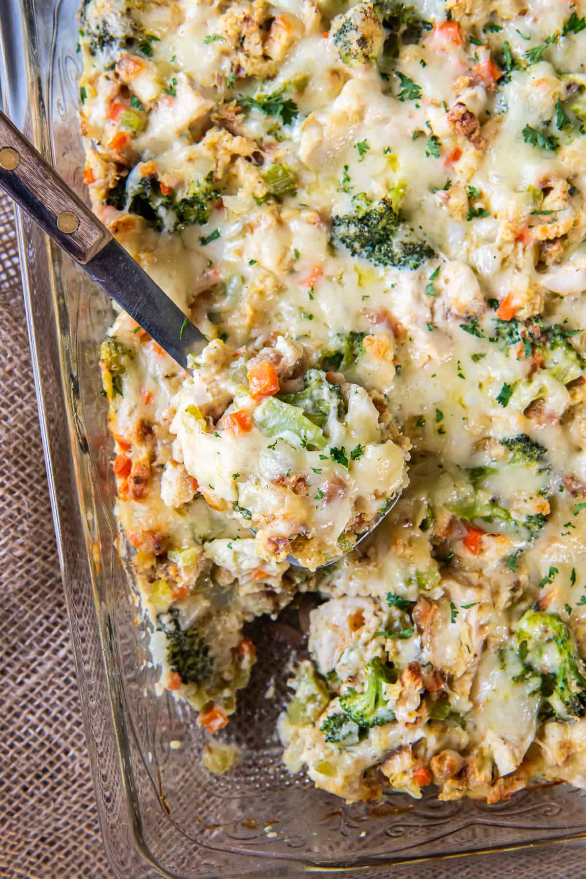 A spoon scooping chicken stuffing bake with broccoli and cheese from a baking dish.