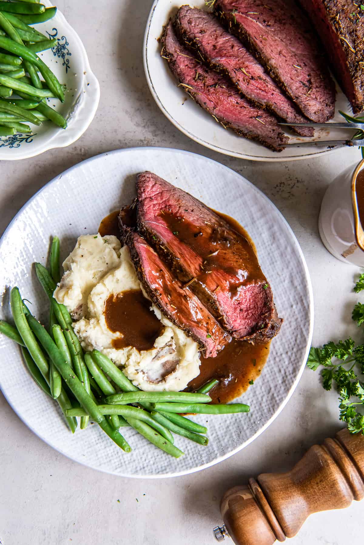 A top down shot of a dinner plate with cross rib roast, mashed potatoes and gravy, and green beans.