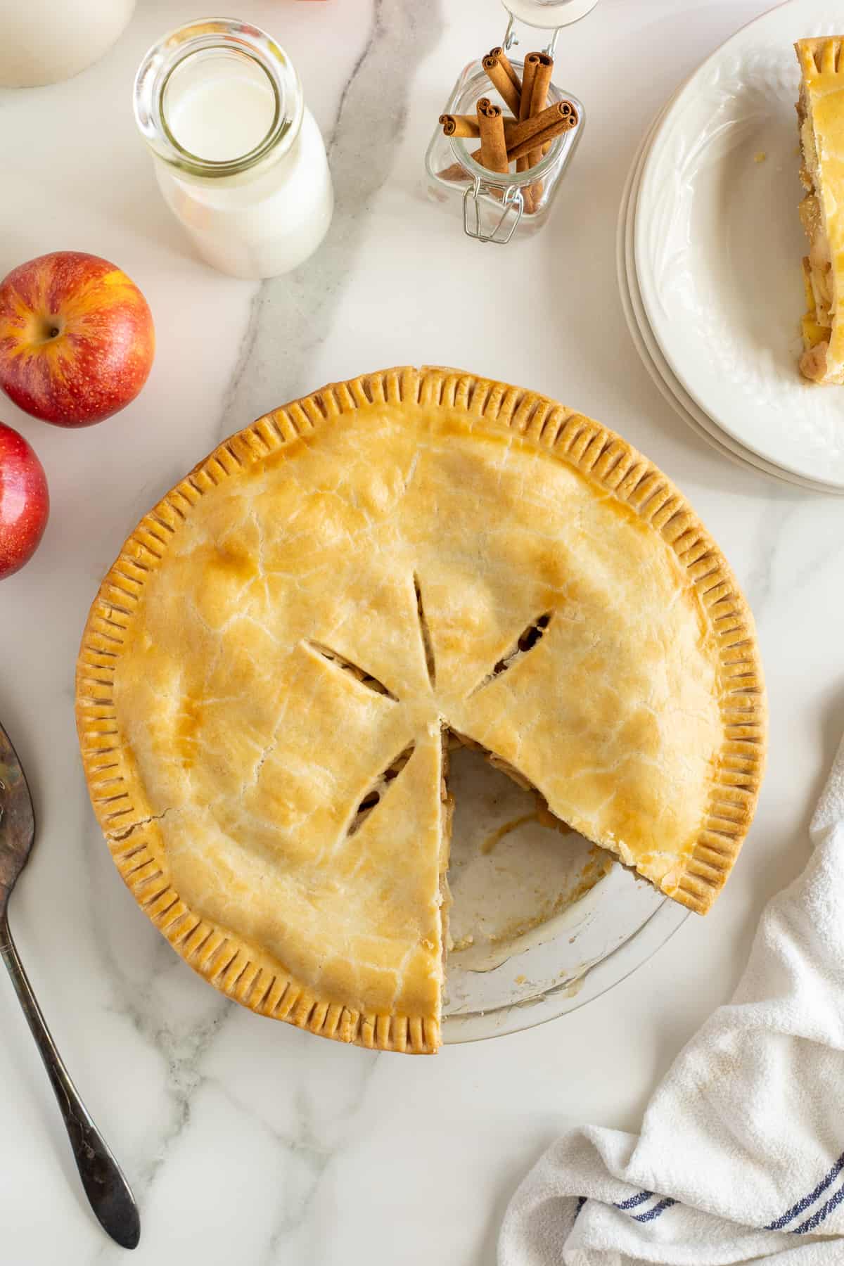 A top down shot of an apple pie with a slice missing on a kitchen counter.