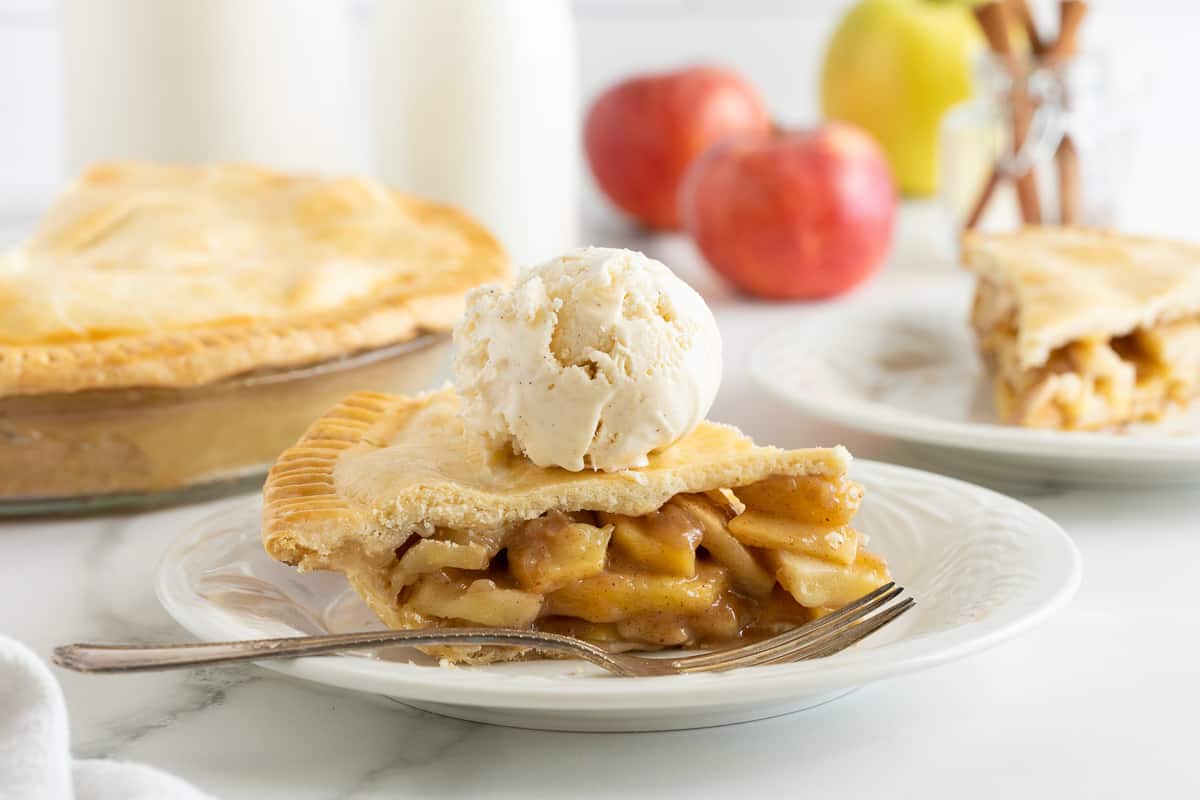 A slice of apple pie topped with a scoop of vanilla ice cream on a plate with a fork.