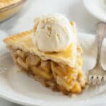 A slice of apple pie topped with a scoop of vanilla ice cream on a plate with a fork.