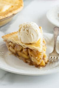 A slice of apple pie topped with a scoop of vanilla ice cream on a plate with a fork.