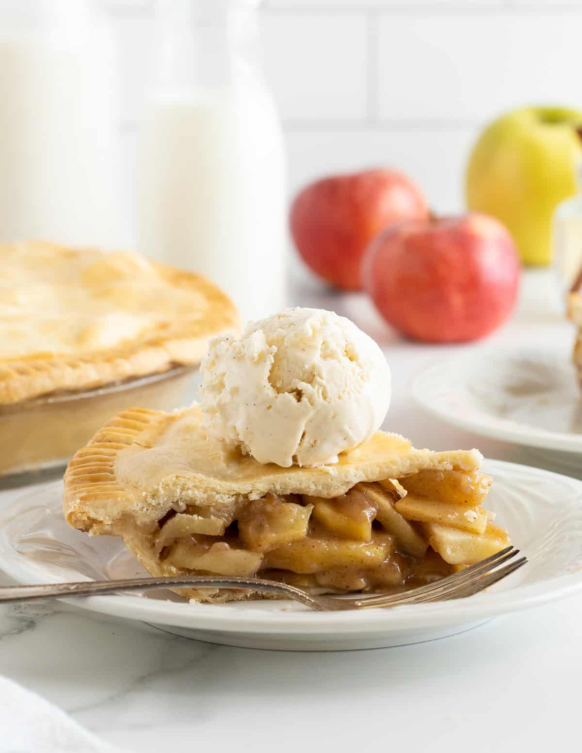 A slice of apple pie topped with a scoop of vanilla ice cream on a plate with a fork.