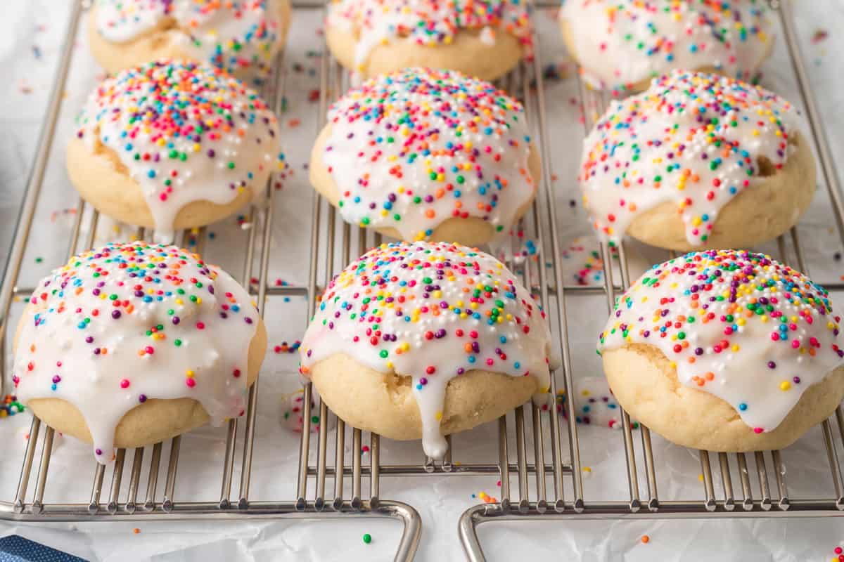 Iced cookies with rainbow sprinkles resting on a wire rack.