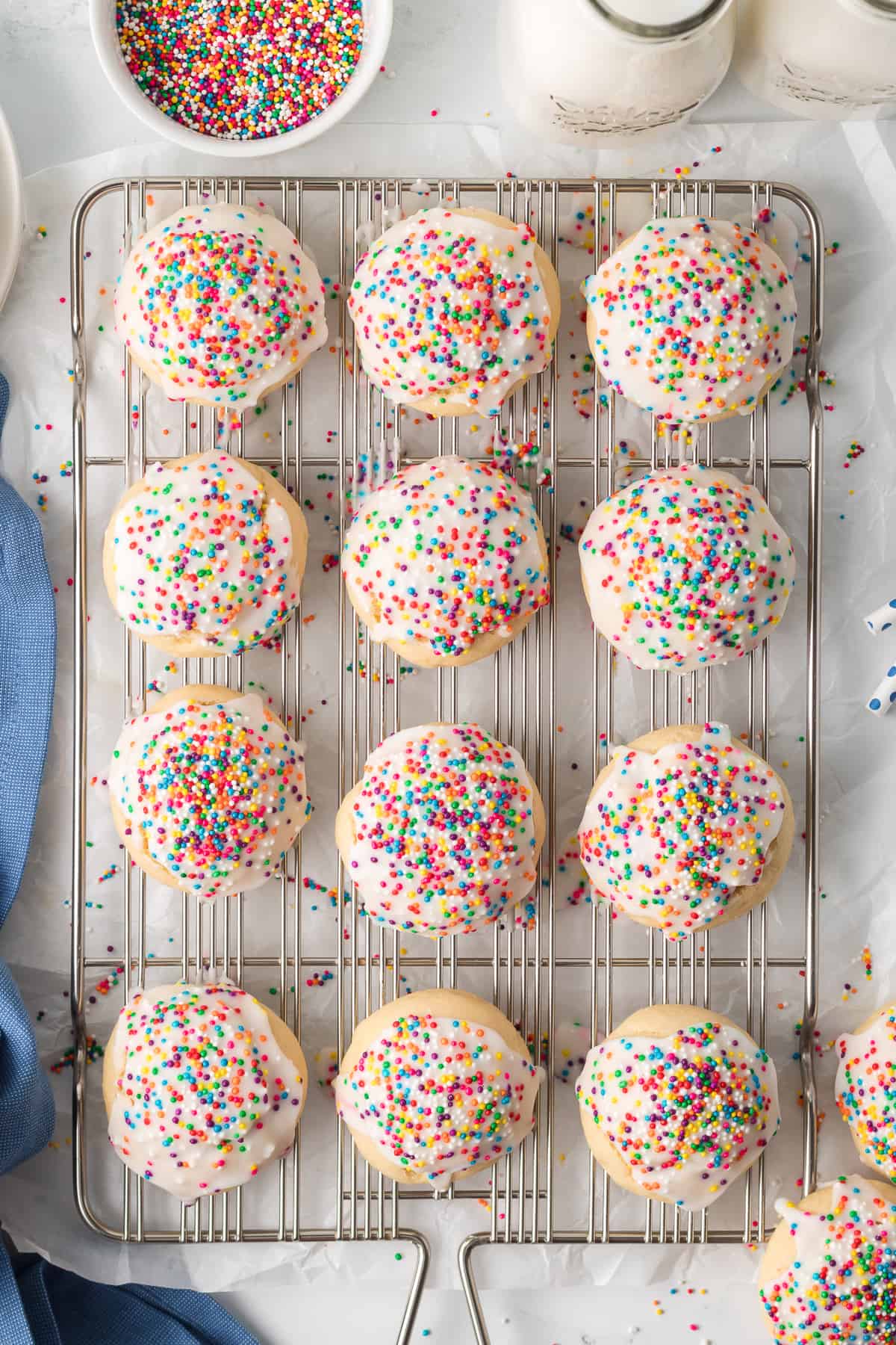 A top down shot of Italian Cookies with icing and rainbow sprinkles on a wire rack.