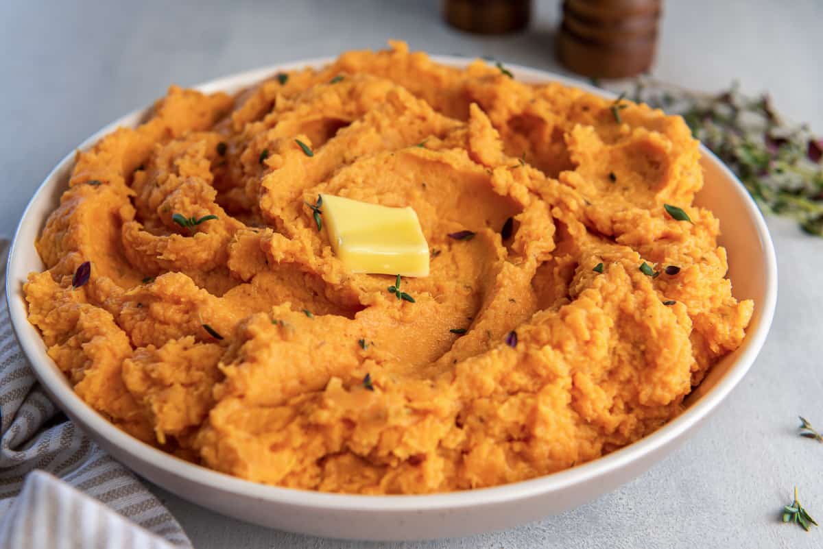 A bowl of mashed sweet potatoes topped with thyme and butter.