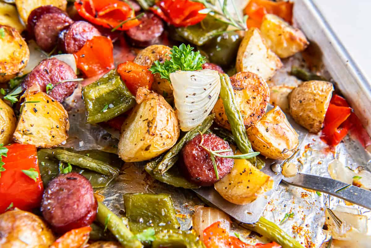 A close up of a spatula resting under oven roasted sausage and potatoes on a sheet pan.