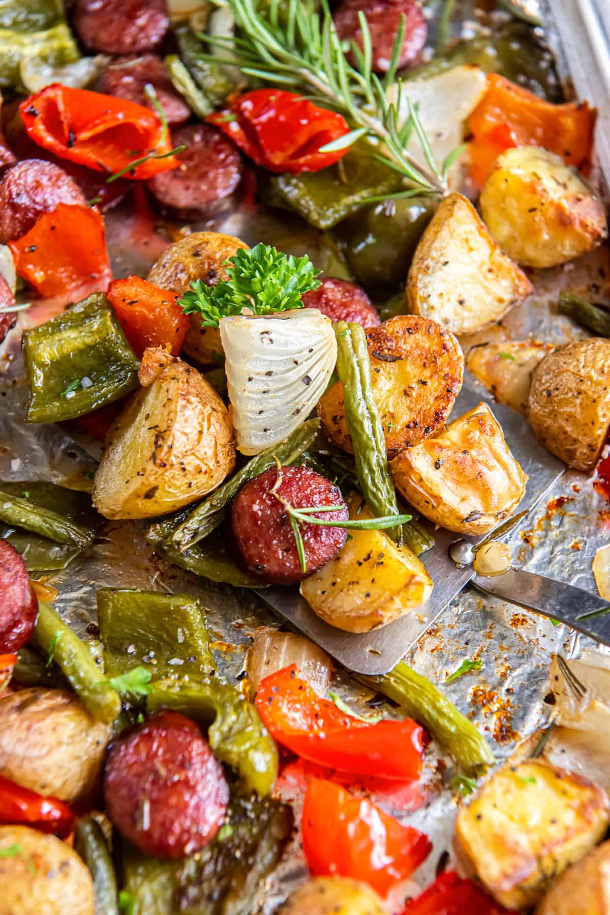 A close up of a spatula resting under oven roasted sausage and potatoes on a sheet pan.