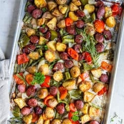 Sausage and potatoes with bell peppers and green beans on a baking sheet.